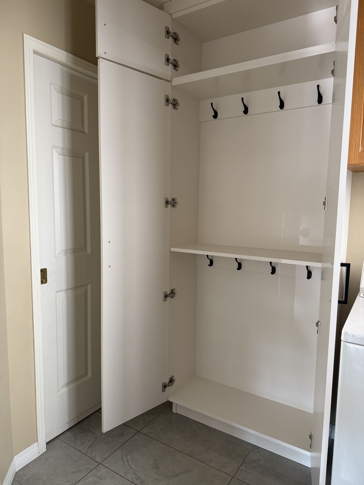 Custom mudroom closet with doors open showing two rows of coat hooks mounted to solid backing